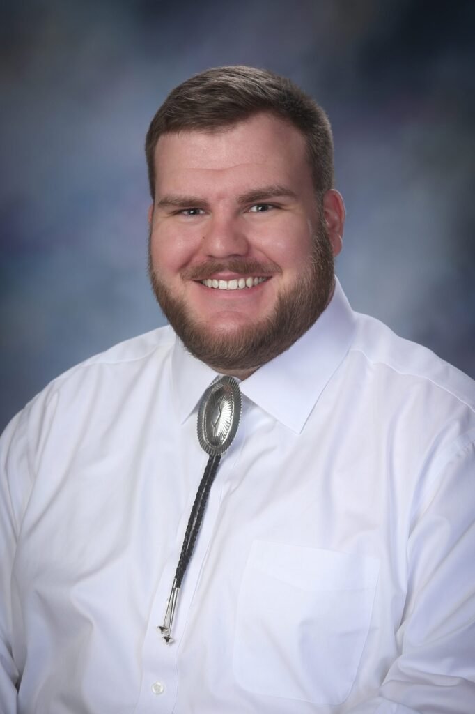 Pastor Noah McCann, a young man with a neat beard wearing a western shirt and bolo tie.